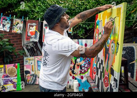 Giovane artista maschile che finì la sua pittura su tela in piedi in un giardino. Foto Stock