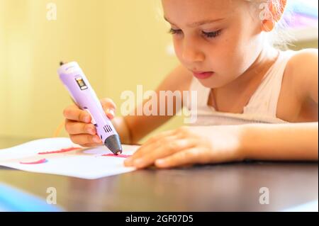 piccola bambina di sette anni disegna con una penna 3d e plastica a casa. creatività e fai da te dei bambini Foto Stock