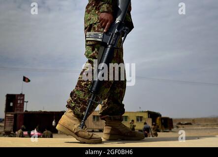 Un soldato dell'esercito nazionale afghano (ANA) custodisce il perimetro con il nome di col. Timothy Lee, 466esimo comandante del gruppo di spedizione aerea e di Airmen Joint Expeditionary mascherati assegnati alla 4a Divisione di fanteria, completare una missione presso il composto di munizioni ANA, provincia di Kandahar, Afghanistan, 13 marzo 2014. In qualità di comandante del convoglio e consulente logistico senior, Buffin ha condotto 12 Airmen sulla base operativa diretta Lindsey e sul compound dell'esercito nazionale afghano durante la missione. Lee, è il comandante di più di 1,500 Airmen assegnati al 466a AES, come Buffin, a sostegno dell'operazione Enduring Freedom in j Foto Stock