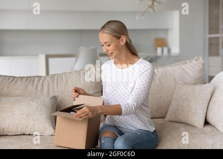 Donna felice disimballaggio contenitore a casa, apertura scatola di cartone Foto Stock