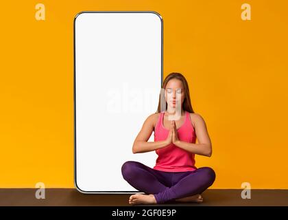 Yogi donna meditating vicino schermo vuoto dello smartphone Foto Stock