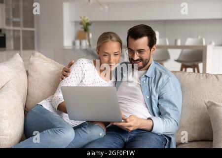 La coppia felice si è concentrata sul portatile seduto insieme sul divano Foto Stock