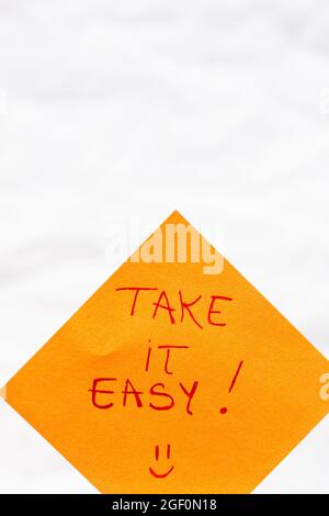 Un testo scritto a mano che dice "Take it easy" su carta arancione Foto Stock