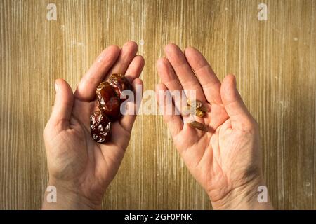 Vista dall'alto di mucchio di frutta di data su una mano di donna e ossa come semi d'altra parte per piantare la palma su sfondo di legno Foto Stock