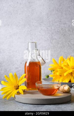 Sciroppo di carciofo di Gerusalemme in bottiglia, fiori e radice su sfondo grigio. Formato verticale. Foto Stock