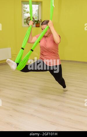 Una giovane ragazza pratica yoga su un'amaca nella sala. La ragazza esegue asana in limbo. Foto Stock