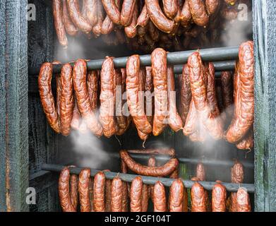 Fumo di salami piccanti kielbasa in legno fumo dettaglio casa. Primo piano di salumi affumicati caldi di carne di maiale e manzo appeso all'interno di affumiceria fatta in casa. Foto Stock