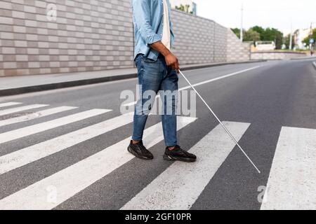 Uomo non riconoscibile per ipovedenti di colore nero con bastone che cammina per la strada della città, primo piano Foto Stock