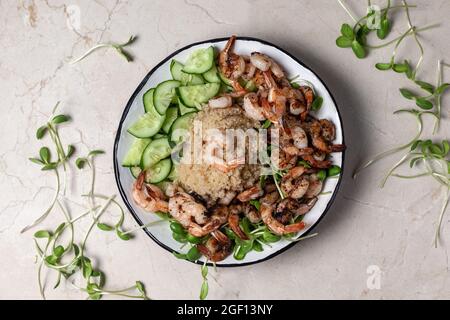 Sana quinoa con gamberi alla griglia o gamberetti, cetrioli e micro verdi sullo sfondo di marmo. Foto Stock
