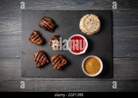 Medaglioni di maiale alla griglia con ketchup e senape su tavola di legno scuro. Foto Stock