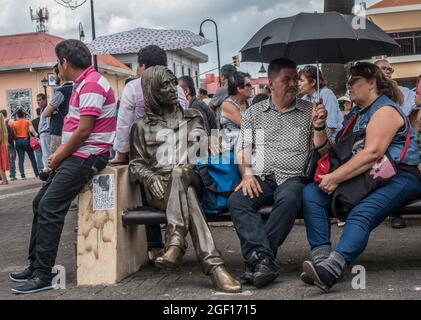 Persone sedute accanto ad una statua di bronzo di John Lennon a San Jose, Costa Rica. Foto Stock