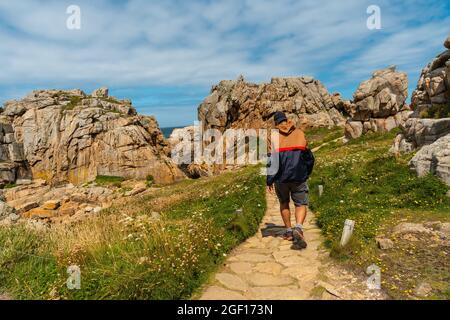 Un maschio che cammina verso una piccola casa Castel Meur tra le rocce vicino al mare in Plougrescant, Francia Foto Stock