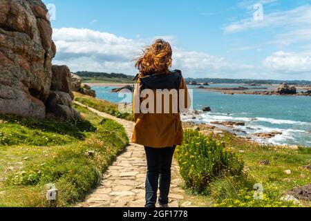 Una femmina che cammina verso una piccola casa Castel Meur tra le rocce vicino al mare in Plougrescant, Francia Foto Stock