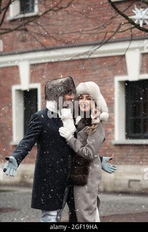 Felice coppia amorevole godere a piedi all'aperto nella neve caduta in città durante le vacanze invernali a Natale Foto Stock