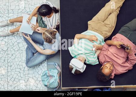 Vista dall'alto in basso in un gruppo di bambini che si rilassano e utilizzano la realtà virtuale durante la pausa alla scuola moderna Foto Stock