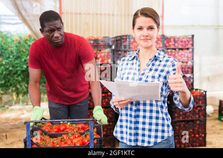 Felice agricoltore femmina che dà i pollici in su in serra magazzino Foto Stock