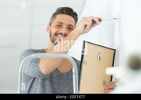 Repairman mettendo cornice immagine sulla parete Foto Stock