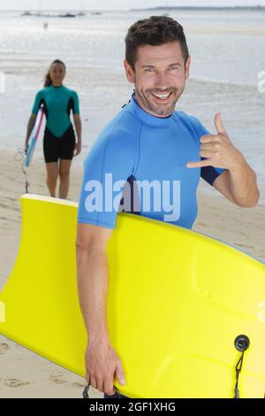 surfista maschile che fa il gesto della mano shaka Foto Stock