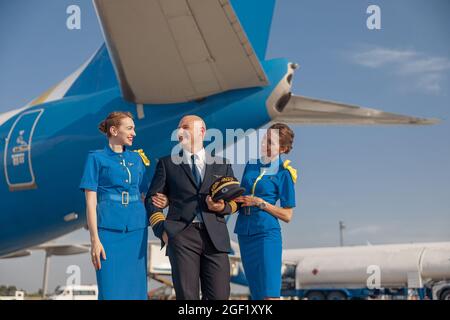 Eccitato pilota con due attraenti stewardesses in piedi insieme davanti ad un aeroplano e sorridente dopo l'atterraggio Foto Stock
