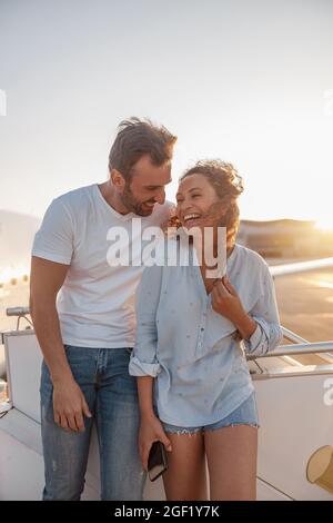 Coppia felice di turisti, uomo e donna che guardano eccitato mentre si levano in piedi all'aperto pronti per salire a bordo dell'aereo al tramonto Foto Stock