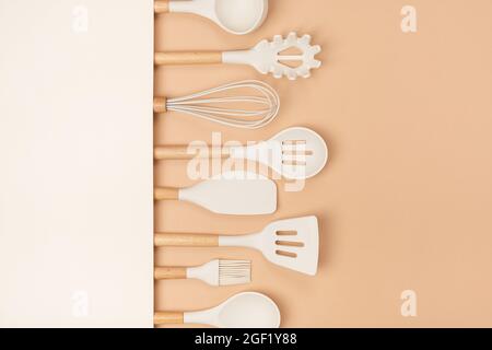 Set utensili da cucina. Utensili da cucina in silicone con manico in legno su sfondo beige con spazio per la copia. Vista dall'alto, disposizione piatta. Foto Stock