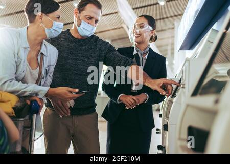 La coppia fa il check-in all'aeroporto con il personale di terra in piedi accanto durante la pandemia. Coppia turistica in maschere facciali al check-in self-service all'airpor Foto Stock
