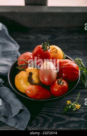 Pomodori multicolore di diverse dimensioni e tipi in un piatto scuro e rustico sfondo di legno Foto Stock