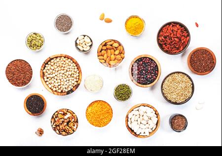 Set di supercibi, legumi, cereali, noci, semi in ciotole su tavola bianca. Spazio di copia, vista dall'alto Foto Stock