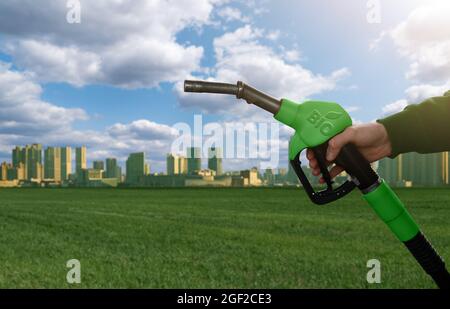 Mano con ugello carburante con iscrizione BIO sullo sfondo verde eco città. Concetto di biocarburante Foto Stock