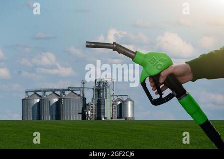 Mano con ugello carburante con iscrizione BIO sullo sfondo dei silos. Concetto di biocarburante Foto Stock