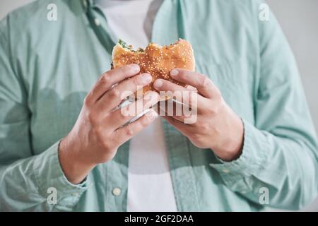 Primo piano dell'uomo che tiene l'hamburger nelle sue mani per mangiarlo per pranzo Foto Stock