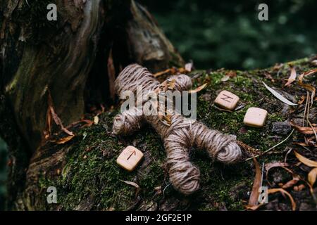 Una bambola voodoo intrecciata di fili, falce e rune in rituale nella foresta misteriosa. Foto Stock