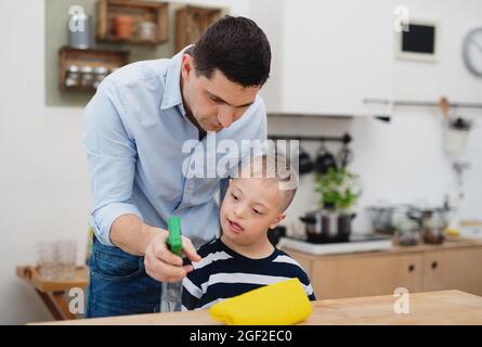 Padre con figlio sindrome di happy down al chiuso in cucina, tavolo di pulizia. Foto Stock