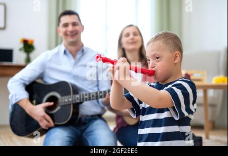 Allegro ragazzo sindrome giù con i genitori che suonano strumenti musicali, ridendo. Foto Stock