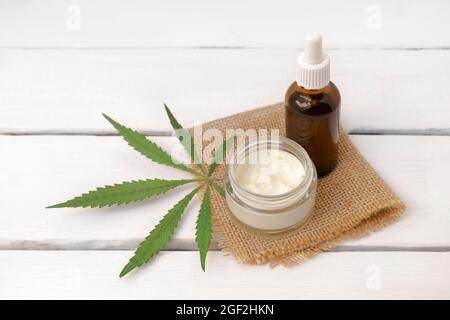 Crema facciale e siero infuso da CBD con foglia verde di cannabis su sfondo bianco di legno con spazio copia Foto Stock