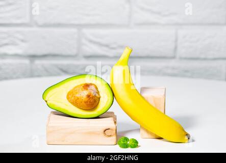 Avocado creativo, banana e micro verde equilibrio legno stand e podi., sfondo bianco, equilibrio sano cibo. Concetto di nutrizione equilibrata. Foto Stock