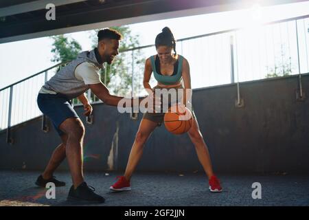 Amici uomini e donne che giocano a basket all'aperto in città. Foto Stock