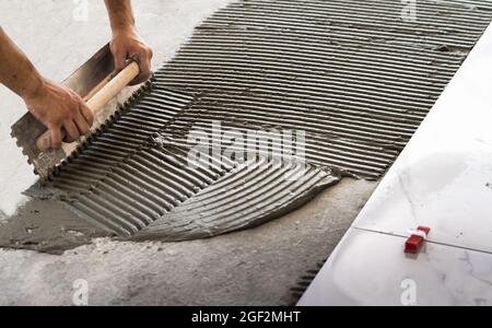 La posa di piastrelle di ceramica. Mortaio Troweling su un pavimento di cemento in preparazione per la posa di pavimento bianco piastrella. Foto Stock