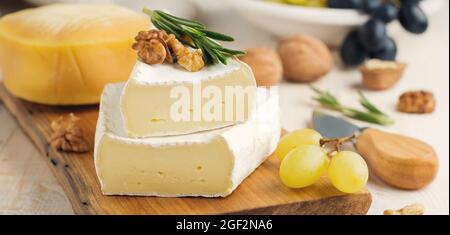 Impilare il Camembert con uva, noci e basilico su cemento grigio chiaro o pietra. Messa a fuoco selettiva. Foto Stock