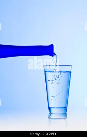 Un bicchiere viene riempito con acqua da una bottiglia blu Foto Stock