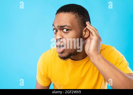 African American Guy Listening mano vicino all'orecchio, sfondo blu Foto Stock