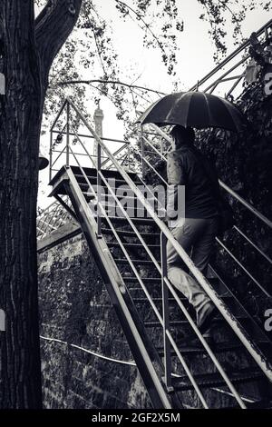 Foto verticale in scala di grigi di un uomo con un ombrello sulle scale di Parigi Foto Stock