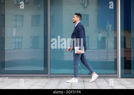 Uomo d'affari arabo allegro con pad a piedi per strada, a tutta lunghezza Foto Stock