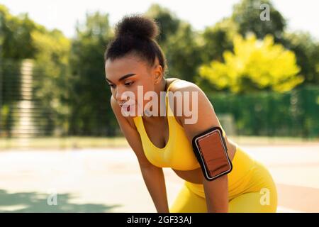 Donna sportiva nera in abbigliamento sportivo giallo riposante dopo la corsa Foto Stock