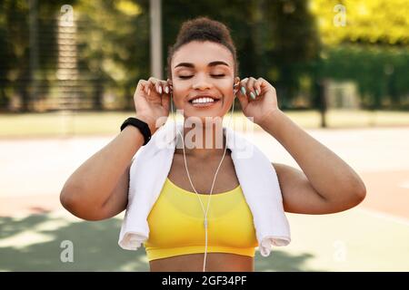 Donna sportiva nera con abbigliamento sportivo giallo indossando le cuffie Foto Stock