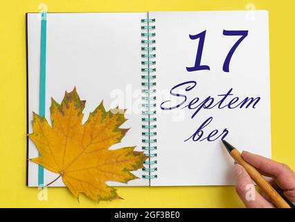 17 settembre. Scrivere a mano la data 17 settembre in un taccuino aperto con una bella foglia di acero naturale su sfondo giallo. Mese autunnale Foto Stock