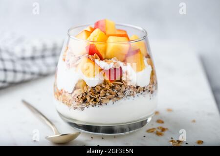 Yogurt granola parfait con cubetti di pesca in vaso di vetro su tavola di marmo bianco, vista da primo piano Foto Stock