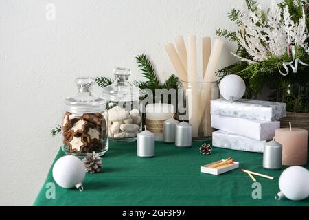 Tavolo natalizio o di Capodanno decorato per le feste, thuja e rami decorativi di abete rosso, candele e palline bianche di Natale, biscotti in un vaso Foto Stock