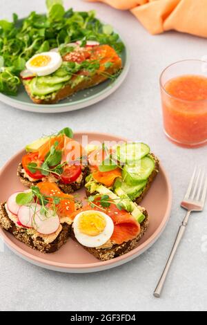 Sana e gustosa colazione, panini con avocado e salmone, cetrioli e pomodori, ravanelli e micrograni di piselli con uova sode e insalata di radice Foto Stock