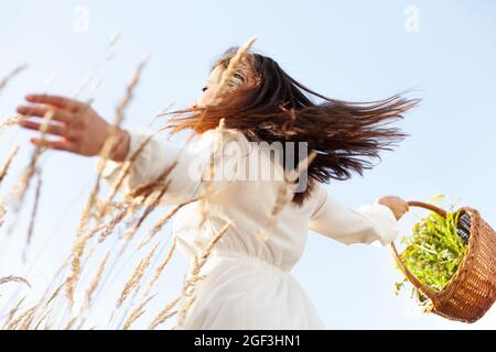 Donna danzante con cesti di vimini nel prato. Raccolta di erbe nel cestello. Scenario positivo. Foto Stock